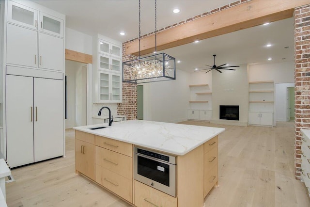 kitchen featuring oven, paneled built in fridge, sink, ceiling fan, and an island with sink