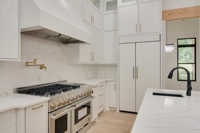 kitchen featuring white cabinets, sink, premium appliances, light stone counters, and custom range hood