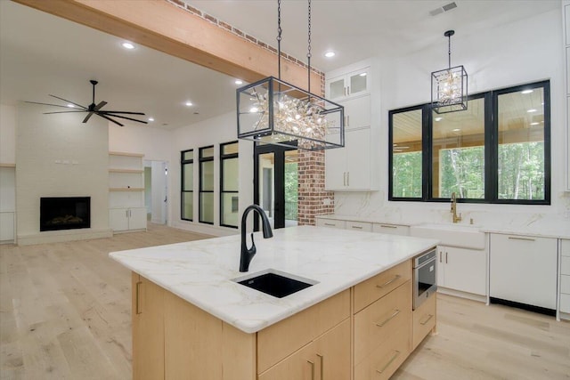 kitchen featuring white cabinets, sink, an island with sink, and hanging light fixtures