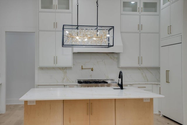 kitchen featuring white cabinets, a center island with sink, light stone counters, and tasteful backsplash