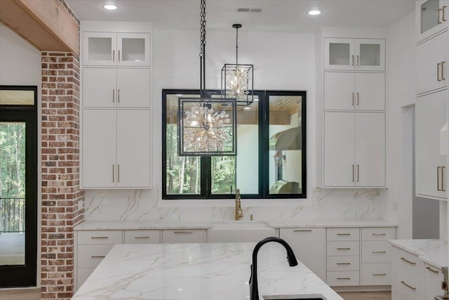 kitchen featuring sink, tasteful backsplash, decorative light fixtures, light stone counters, and white cabinetry