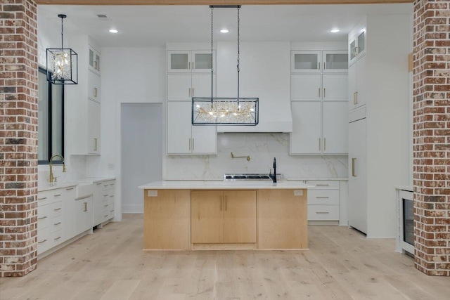 kitchen with decorative light fixtures, a center island with sink, white cabinetry, and light hardwood / wood-style flooring