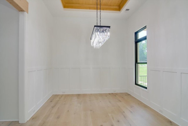 empty room featuring a chandelier, light wood-type flooring, and a tray ceiling