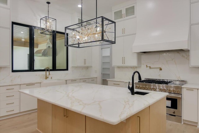 kitchen with hanging light fixtures, high end stainless steel range, a center island with sink, white cabinets, and custom range hood