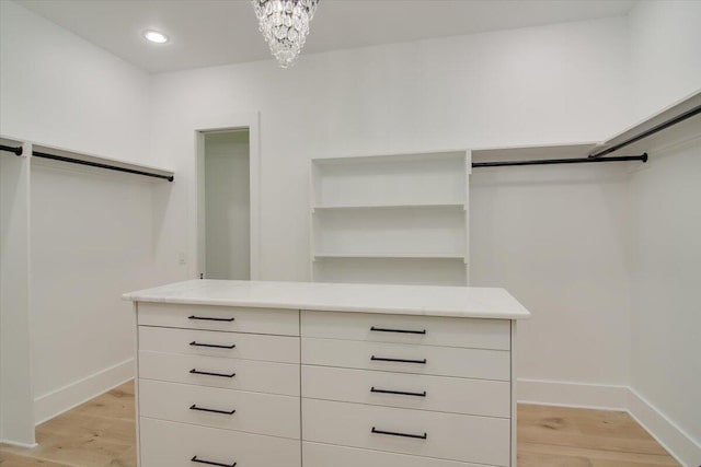 spacious closet featuring light wood-type flooring and an inviting chandelier