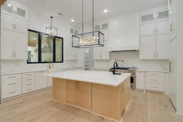 kitchen with high end stove, white cabinetry, a center island with sink, and light wood-type flooring