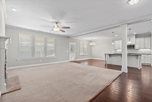 unfurnished living room featuring a brick fireplace, ornamental molding, a textured ceiling, ceiling fan with notable chandelier, and dark wood-type flooring