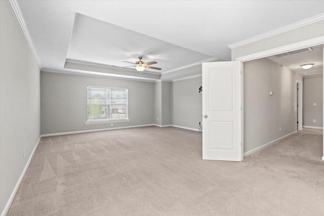 spare room with a tray ceiling, light carpet, ceiling fan, and ornamental molding