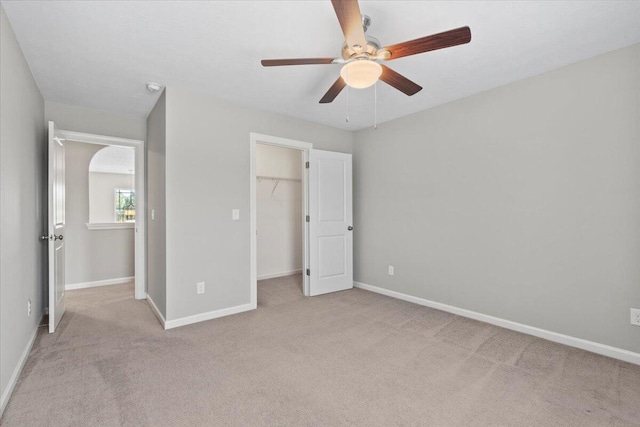 unfurnished bedroom featuring a closet, light colored carpet, a spacious closet, and ceiling fan