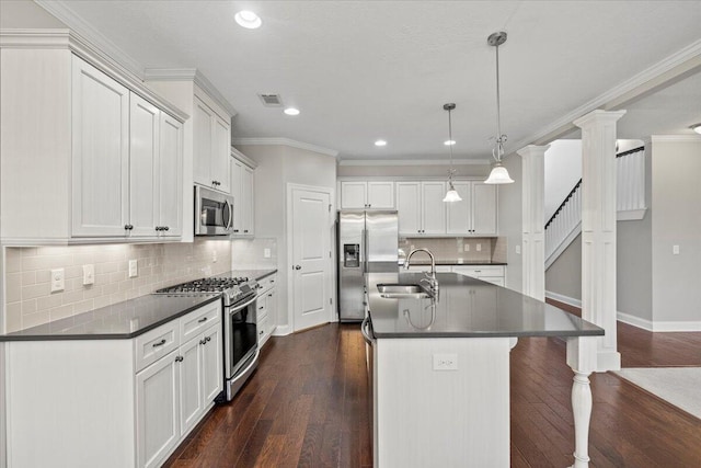 kitchen featuring stainless steel appliances, sink, white cabinetry, hanging light fixtures, and an island with sink