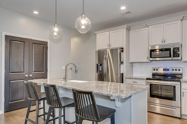 kitchen featuring a sink, stainless steel appliances, tasteful backsplash, and light wood-style flooring