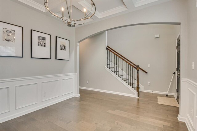 foyer featuring a notable chandelier, coffered ceiling, wood finished floors, arched walkways, and a decorative wall