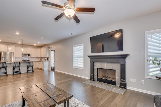 living room featuring ceiling fan, baseboards, recessed lighting, a fireplace, and dark wood-style flooring