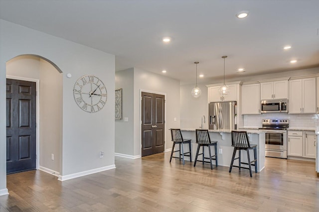 kitchen featuring wood finished floors, arched walkways, appliances with stainless steel finishes, a kitchen bar, and backsplash