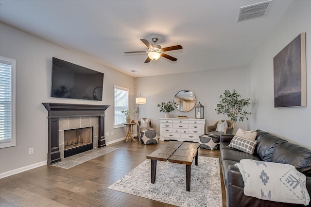 living area featuring wood finished floors, a ceiling fan, visible vents, baseboards, and a fireplace