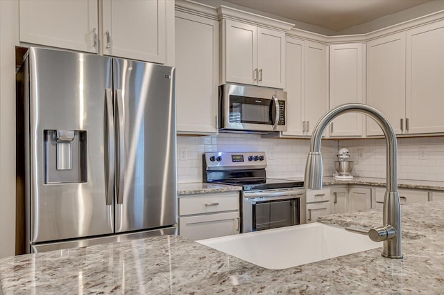 kitchen featuring decorative backsplash, light stone counters, appliances with stainless steel finishes, and a sink