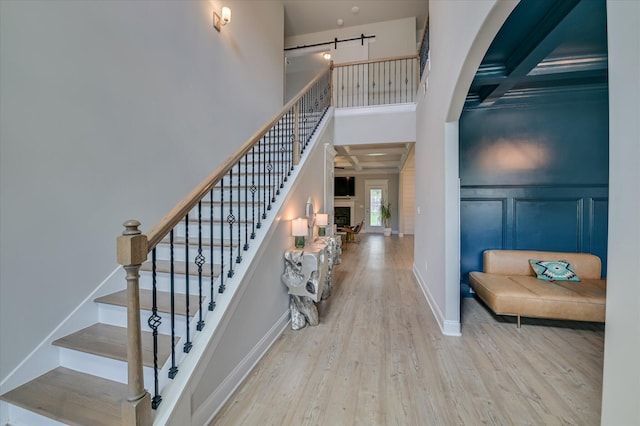 staircase with wood finished floors, a barn door, a decorative wall, beamed ceiling, and a high ceiling