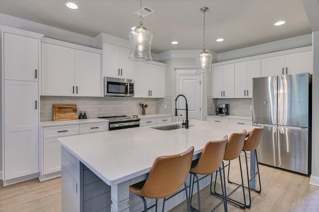 kitchen with stainless steel appliances, a sink, crown molding, white cabinetry, and an island with sink