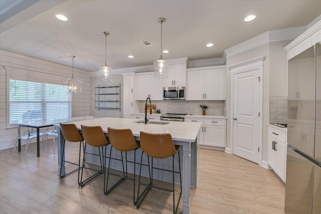 kitchen featuring stainless steel appliances, a breakfast bar area, a sink, light wood-type flooring, and a kitchen island with sink