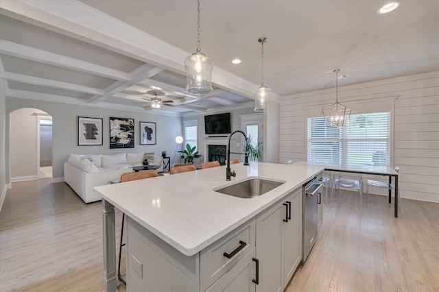 kitchen with a sink, coffered ceiling, dishwasher, a center island with sink, and light wood-style flooring