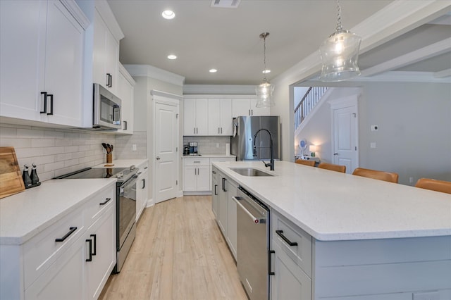 kitchen featuring appliances with stainless steel finishes, a sink, light wood-style flooring, an island with sink, and decorative backsplash
