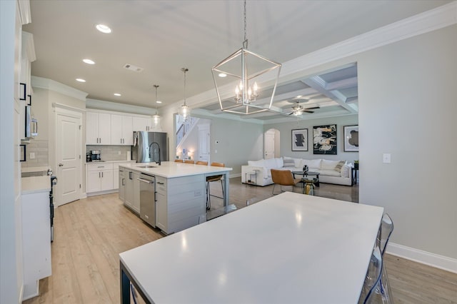 kitchen with appliances with stainless steel finishes, a sink, baseboards, a center island with sink, and light wood-style flooring