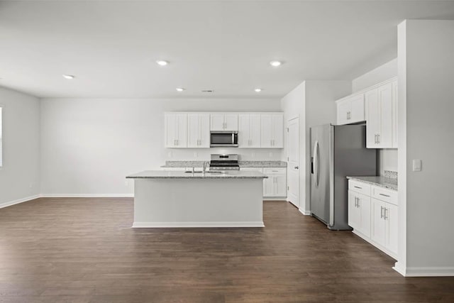 kitchen with light stone countertops, stainless steel appliances, white cabinetry, and a center island with sink