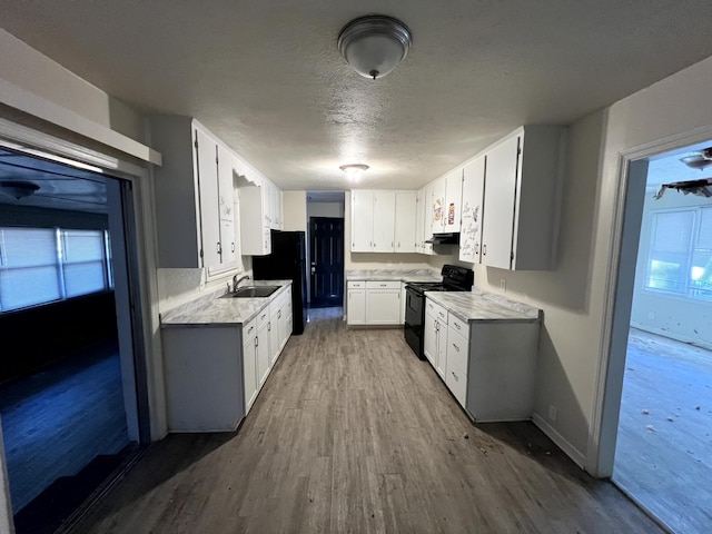 kitchen with black electric range oven, sink, a textured ceiling, white cabinetry, and wood-type flooring