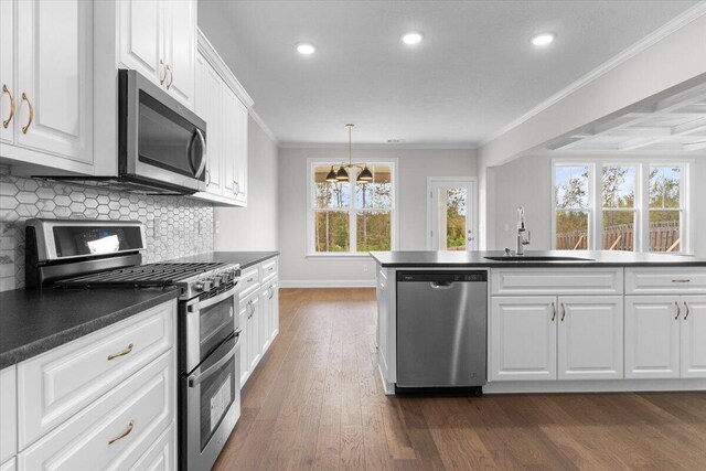 kitchen with dark countertops, white cabinetry, crown molding, appliances with stainless steel finishes, and a sink