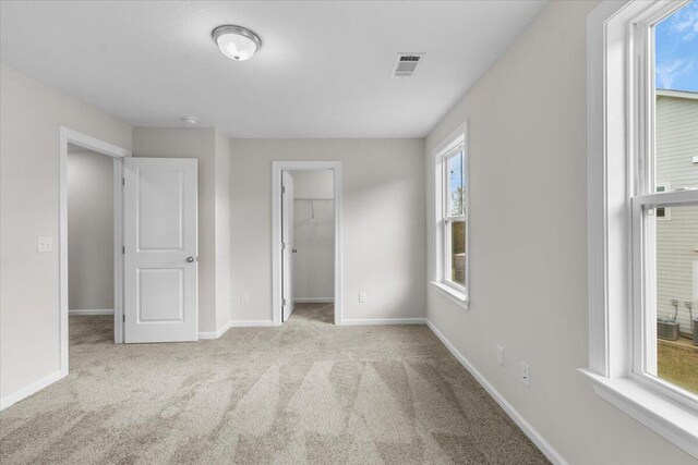 unfurnished bedroom with light colored carpet, visible vents, a spacious closet, and baseboards