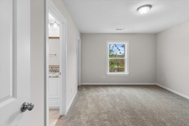 spare room featuring a textured ceiling, baseboards, light colored carpet, and visible vents