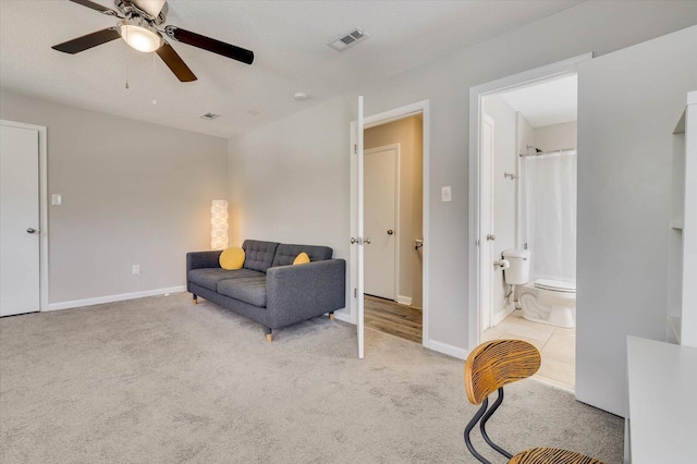 living area with a textured ceiling, light colored carpet, and ceiling fan