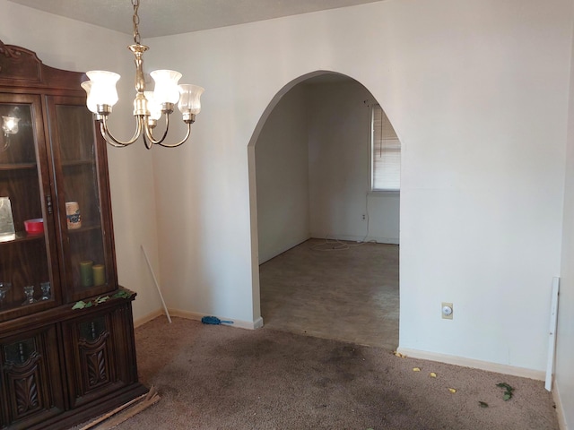 empty room with a notable chandelier, carpet flooring, baseboards, and arched walkways