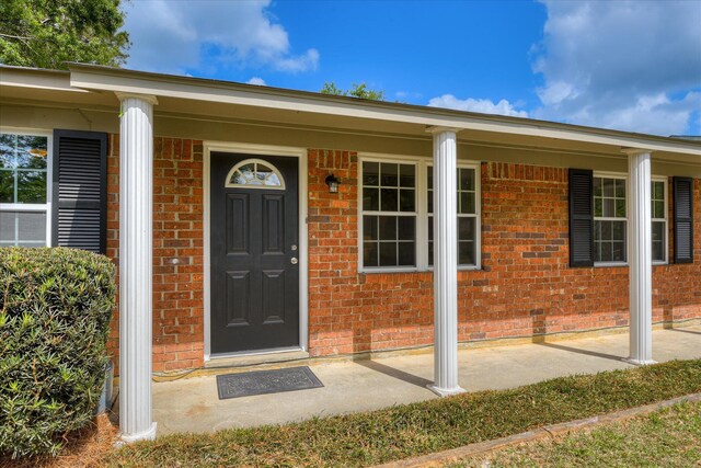 view of exterior entry with brick siding and covered porch