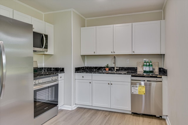 kitchen featuring light wood-style floors, dark stone counters, white cabinets, a sink, and stainless steel appliances