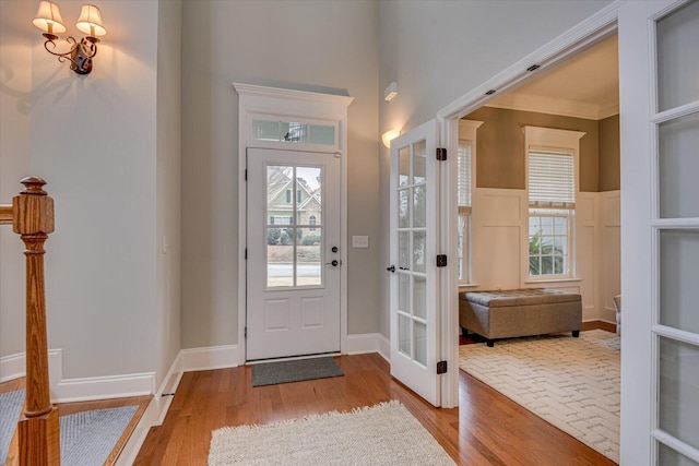 foyer featuring light wood-type flooring, ornamental molding, a wealth of natural light, and french doors