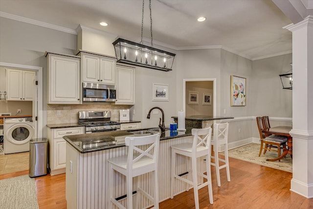 kitchen with a kitchen island with sink, a kitchen breakfast bar, hanging light fixtures, washer / dryer, and stainless steel appliances