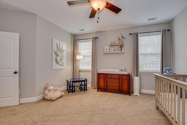 bedroom with light carpet, ceiling fan, and a nursery area