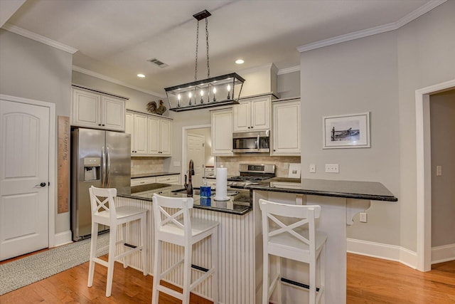 kitchen with appliances with stainless steel finishes, tasteful backsplash, a breakfast bar, decorative light fixtures, and light hardwood / wood-style flooring