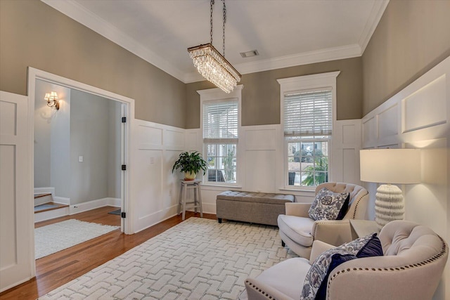 living room with light wood-type flooring, an inviting chandelier, a healthy amount of sunlight, and crown molding