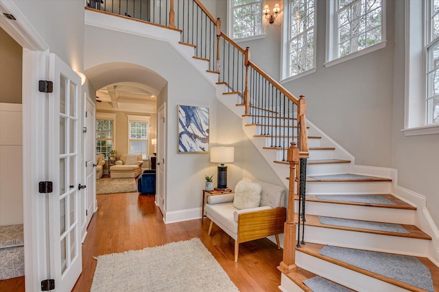 stairway featuring coffered ceiling, beamed ceiling, crown molding, a towering ceiling, and wood-type flooring