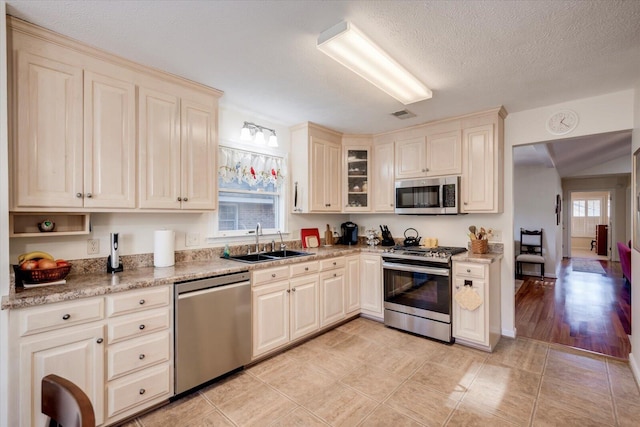 kitchen with a textured ceiling, sink, stainless steel appliances, and cream cabinetry