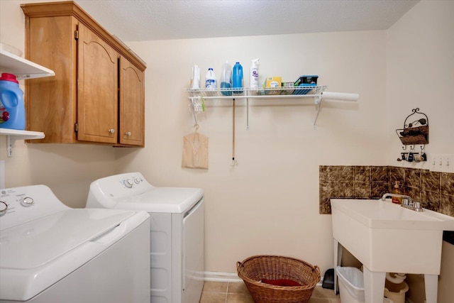 clothes washing area with sink, cabinets, a textured ceiling, washer and clothes dryer, and light tile patterned floors