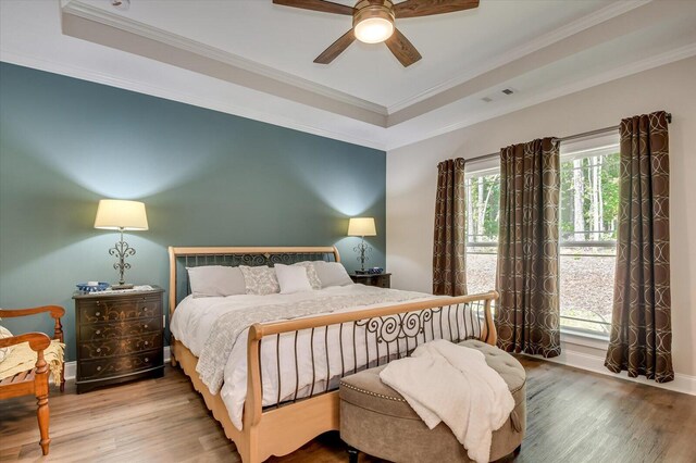 bedroom with ceiling fan, wood-type flooring, crown molding, and a tray ceiling