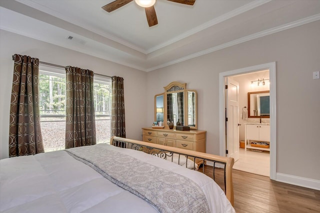 bedroom featuring a raised ceiling, crown molding, hardwood / wood-style flooring, ceiling fan, and connected bathroom