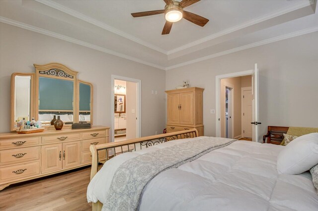 bedroom featuring ceiling fan, a raised ceiling, ensuite bathroom, crown molding, and light wood-type flooring