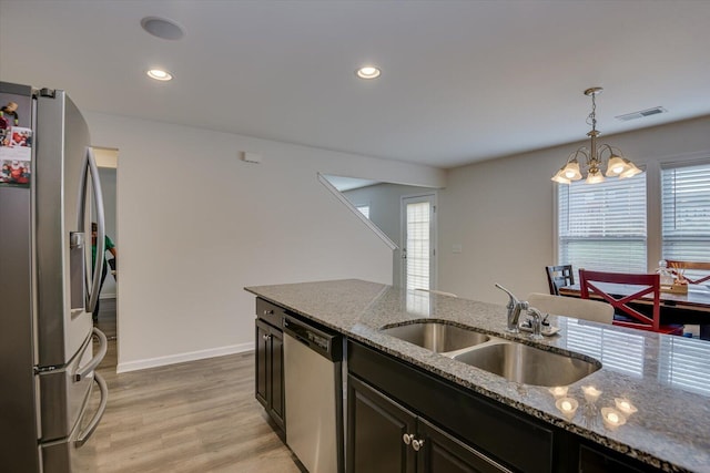 kitchen featuring sink, hanging light fixtures, light stone counters, a notable chandelier, and appliances with stainless steel finishes