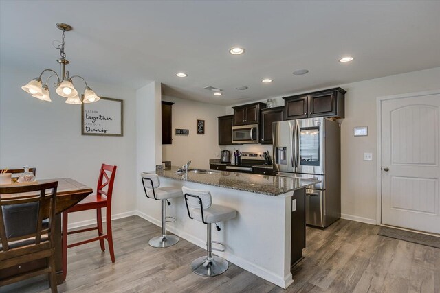 kitchen featuring hanging light fixtures, stainless steel appliances, an inviting chandelier, kitchen peninsula, and dark stone countertops