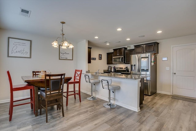 kitchen featuring stainless steel appliances, kitchen peninsula, decorative light fixtures, a breakfast bar area, and light wood-type flooring