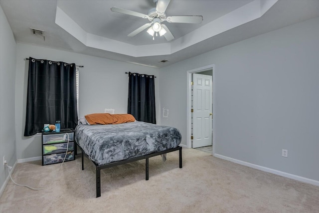 bedroom featuring a raised ceiling, ceiling fan, and light carpet